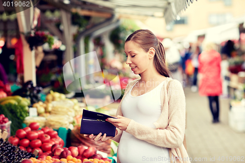 Image of pregnant woman with wallet buying food at market