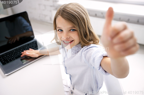 Image of smiling girl with laptop showing thumbs up at home