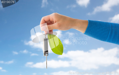 Image of close up of hand holding car key with green leaf