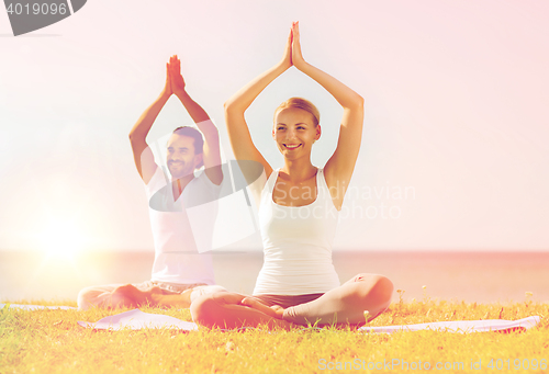 Image of smiling couple making yoga exercises outdoors