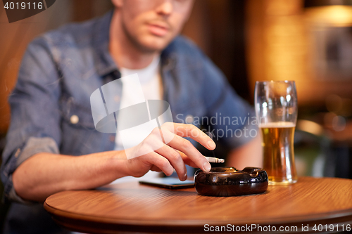Image of man drinking beer and smoking cigarette at bar
