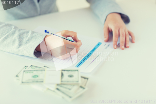 Image of close up of hands with money filling tax form