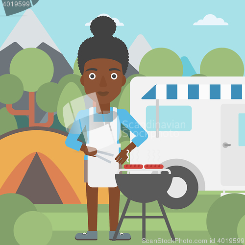Image of Woman having barbecue in front of camper van.