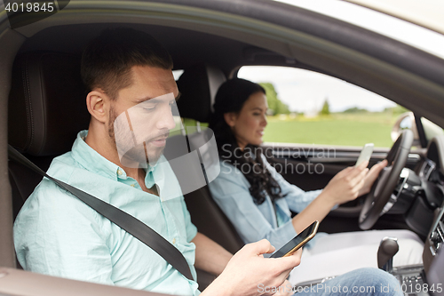 Image of man and woman with smartphones driving in car
