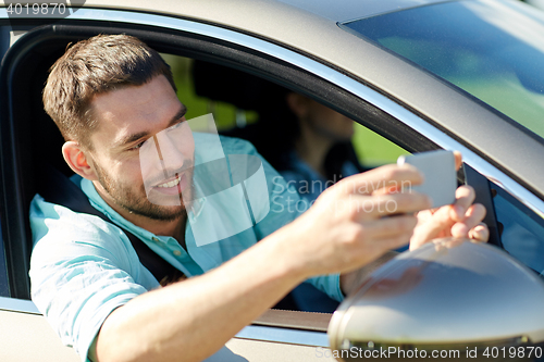 Image of happy smiling man with smartphone driving in car