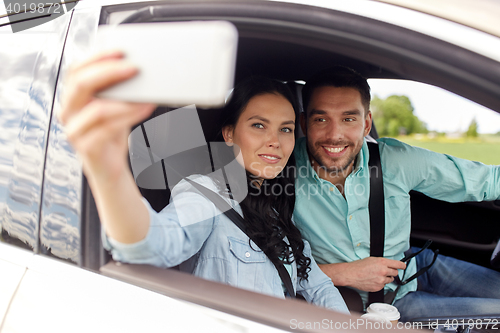 Image of happy couple in car taking selfie with smartphone