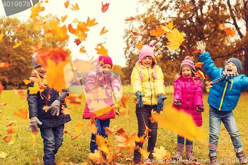 Image of happy children playing with autumn leaves in park