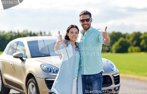 Image of happy man and woman showing thumbs up at car