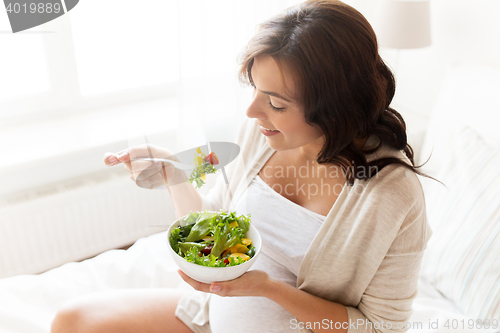 Image of happy pregnant woman eating salad at home