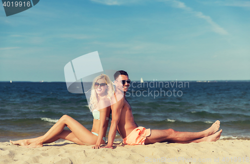 Image of happy couple in swimwear sitting on summer beach