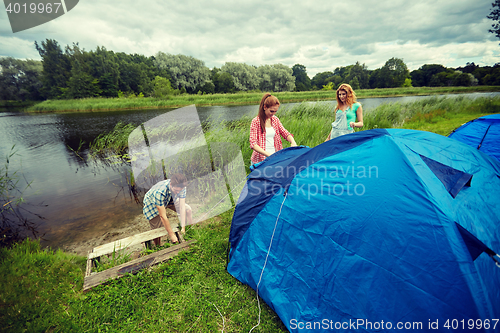 Image of group of smiling friends setting up tent outdoors