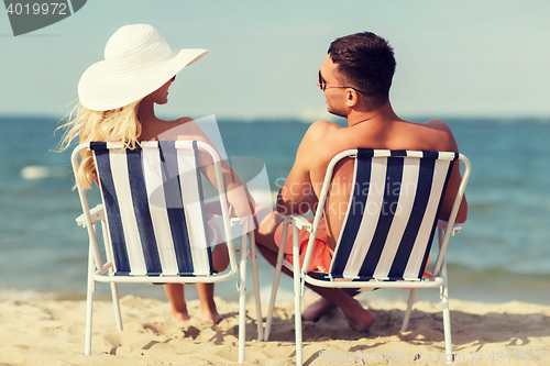 Image of happy couple sunbathing in chairs on summer beach