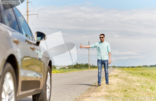 Image of man hitchhiking and stopping car at countryside