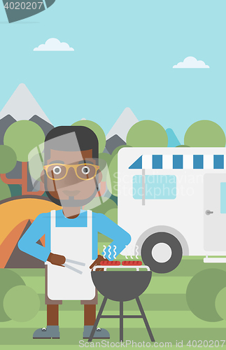 Image of Man having barbecue in front of camper van.