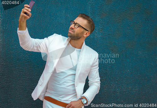 Image of Young man in white clothes taking selfie, stylish portrait