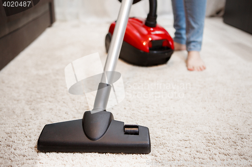 Image of Woman doing cleaning in room, vacuuming white carpet. Image of female foot, red vacuum cleaner and black head of vacuum cleaner closeup
