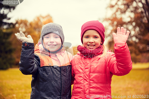 Image of happy girl and boy waving hands in autumn park