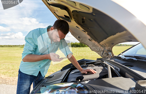 Image of man with smartphone and broken car at countryside