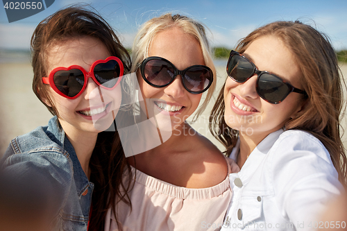 Image of group of smiling women taking selfie on beach