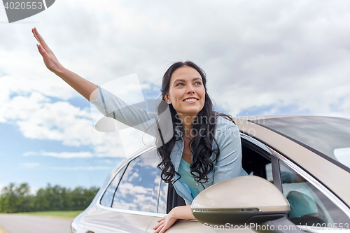 Image of happy young woman driving in car and waving hand