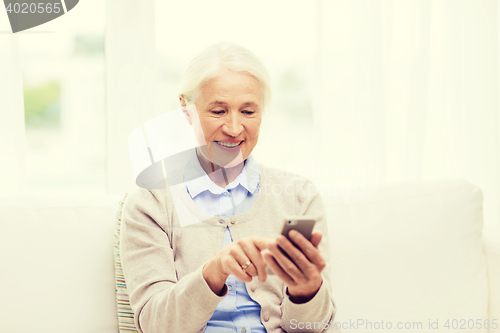 Image of senior woman with smartphone texting at home