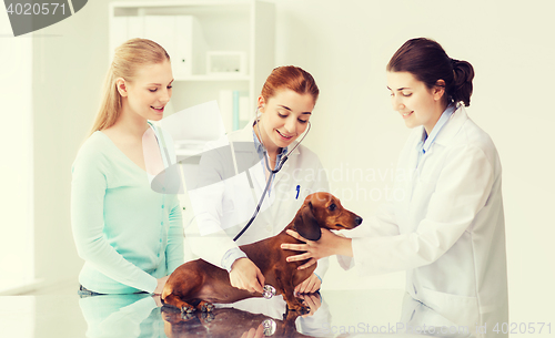 Image of happy woman with dog and doctor at vet clinic