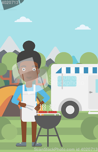 Image of Woman having barbecue in front of camper van.