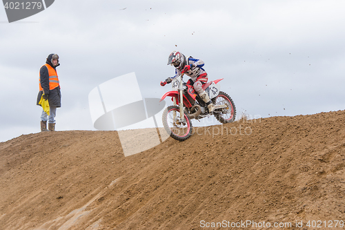 Image of Volgograd, Russia - April 19, 2015: Motorcycle racer moves over the hill, a volunteer was looking at him, at the stage of the Open Championship Motorcycle Cross Country Cup Volgograd Region Governor