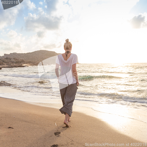 Image of Woman walking on sand beach at golden hour