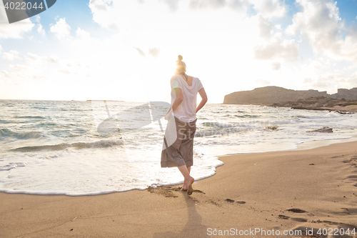 Image of Woman walking on sand beach at golden hour