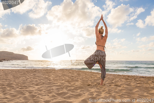 Image of Woman practicing yoga on sea beach at sunset.