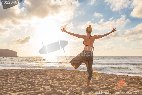 Image of Woman practicing yoga on sea beach at sunset.