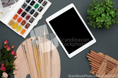 Image of The workspace of artist with laptop, paints, paintbrushes, flowers on black