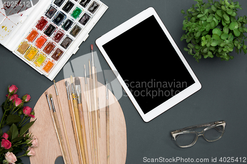 Image of The workspace of artist with laptop, paints, paintbrushes, flowers on black