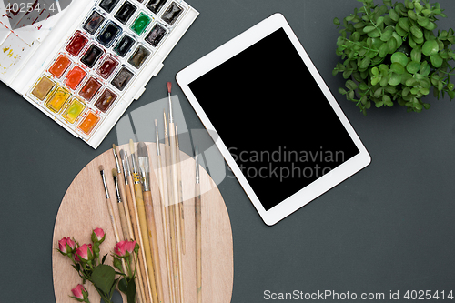 Image of The workspace of artist with laptop, paints, paintbrushes, flowers on black