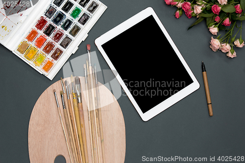 Image of The workspace of artist with laptop, paints, paintbrushes, flowers on black