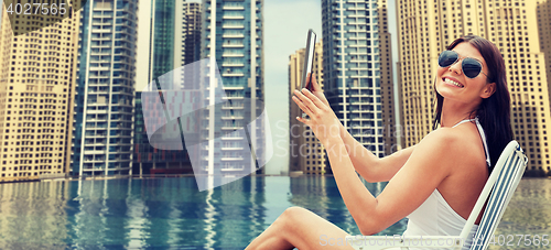 Image of woman with tablet pc sunbathing over city pool