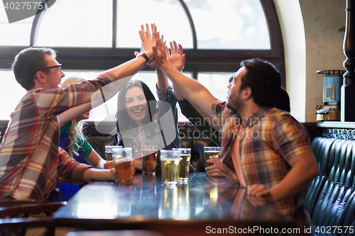 Image of happy friends with beer making high five at pub