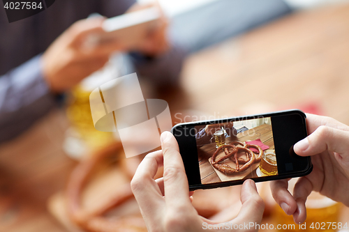 Image of close up of hands picturing pretzel by smartphone