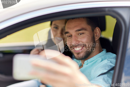 Image of happy couple in car taking selfie with smartphone