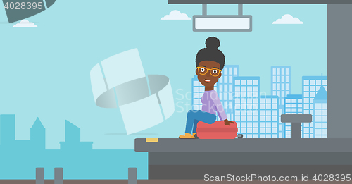 Image of Woman sitting on suitcase at the train station.