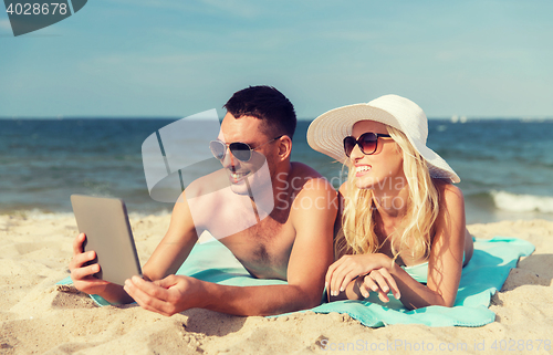 Image of happy couple with tablet pc sunbathing on beach