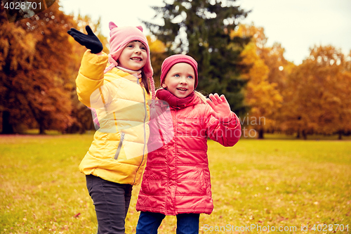 Image of two happy little girls waving hand in autumn park