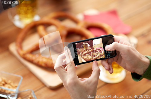 Image of close up of hands picturing pretzel by smartphone