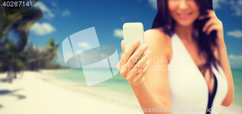 Image of young woman taking selfie with smartphone on beach