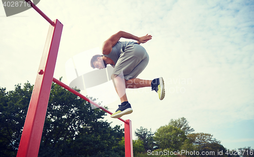 Image of young man jumping on horizontal bar outdoors