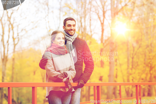 Image of smiling couple hugging on bridge in autumn park