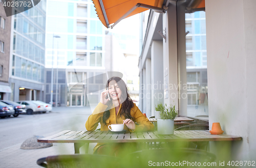 Image of happy woman calling on smartphone at city cafe