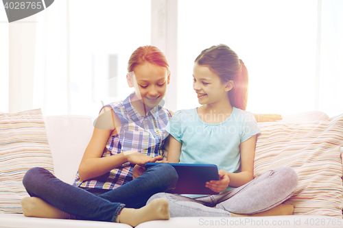 Image of happy girls with tablet pc sitting on sofa at home