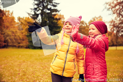 Image of two happy little girls waving hand in autumn park
